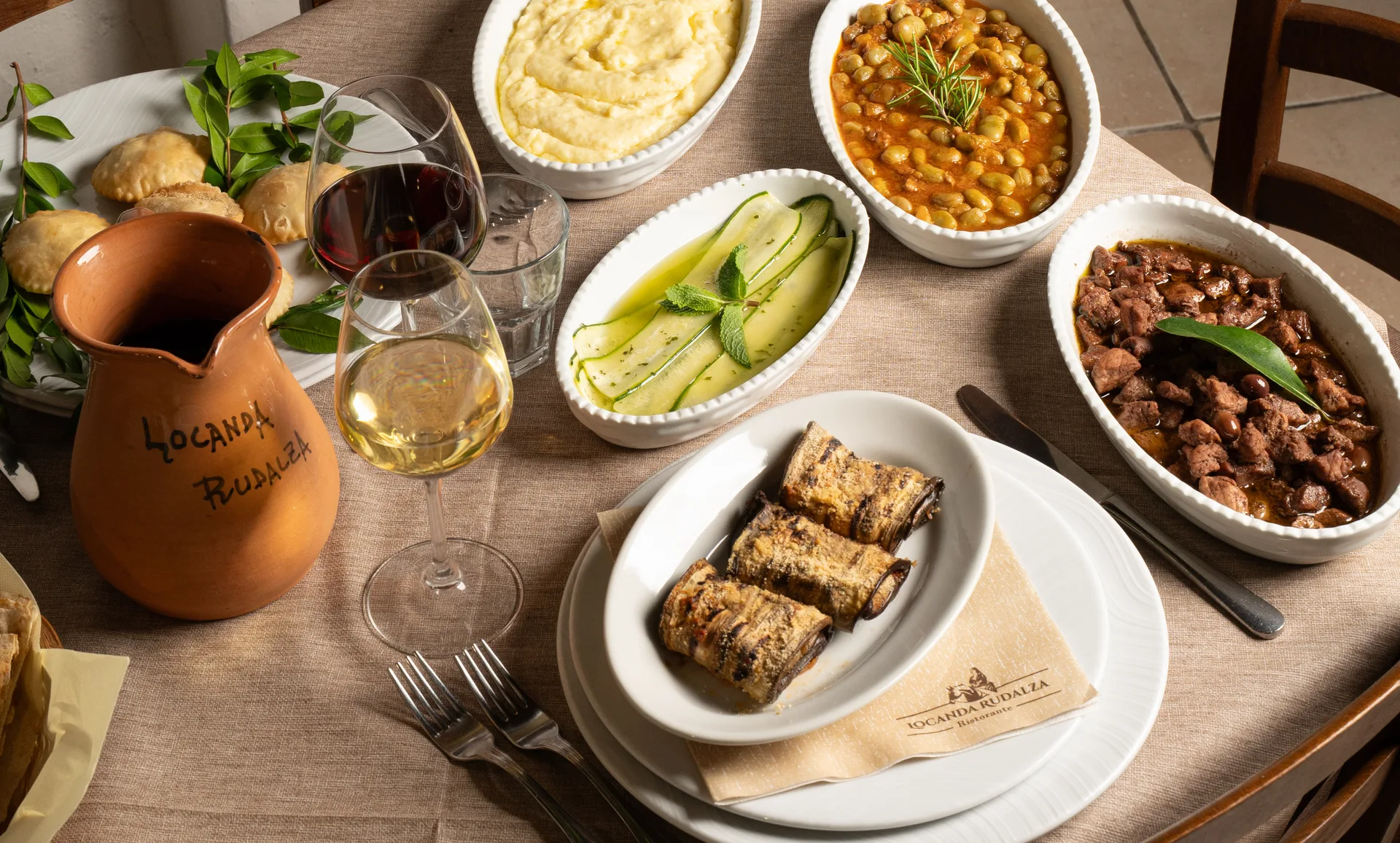 A table of traditional Sardinian dishes at Locanda Rudalza, with a carafe and wine glasses